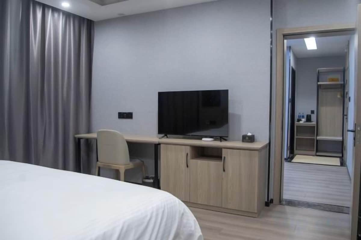 Ein Hotelzimmer mit einem Bett, einem Schreibtisch mit Fernseher, einem Sessel und einem Kleiderschrank.