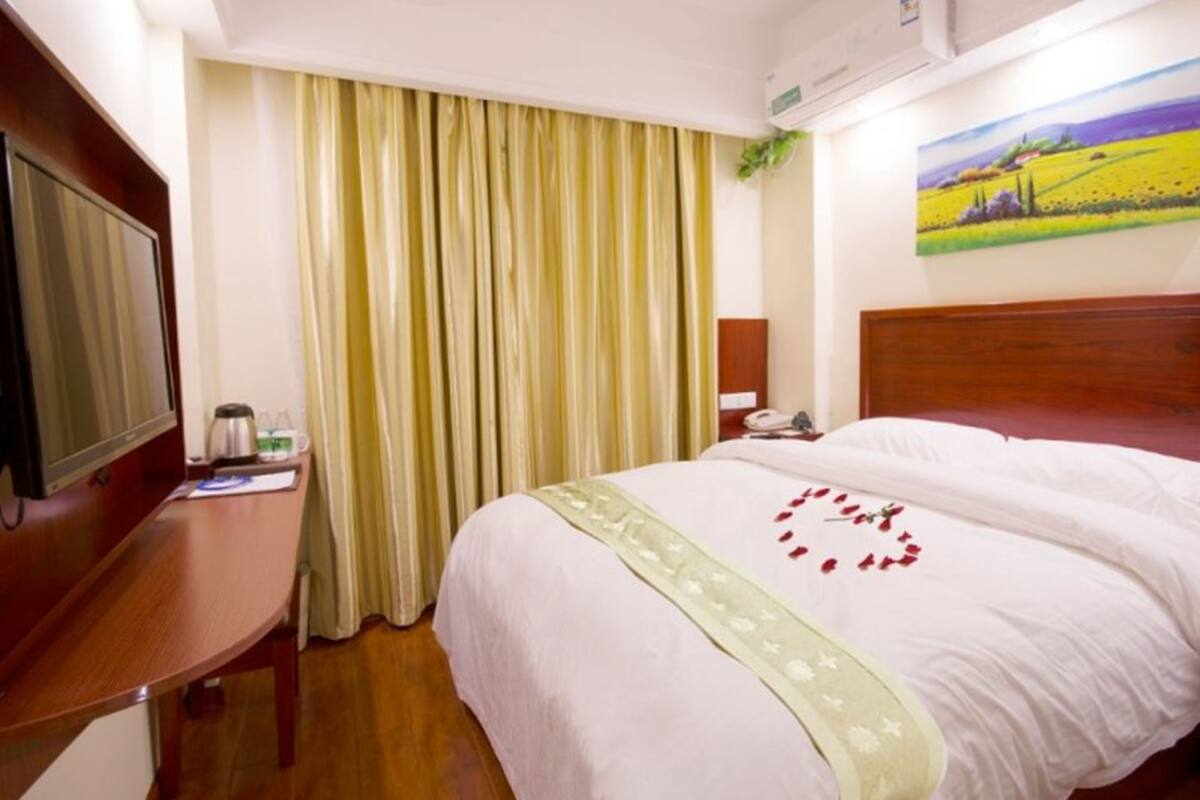 A hotel room with a bed, a desk, a television, a telephone, and a painting on the wall.