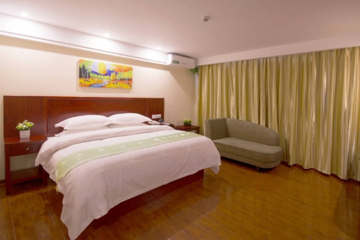 A hotel room with a large bed, a sofa, a painting on the wall, and a curtain.