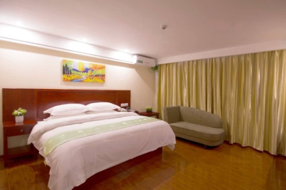 A hotel room with a bed, a nightstand, a sofa, a painting on the wall, and a curtain.