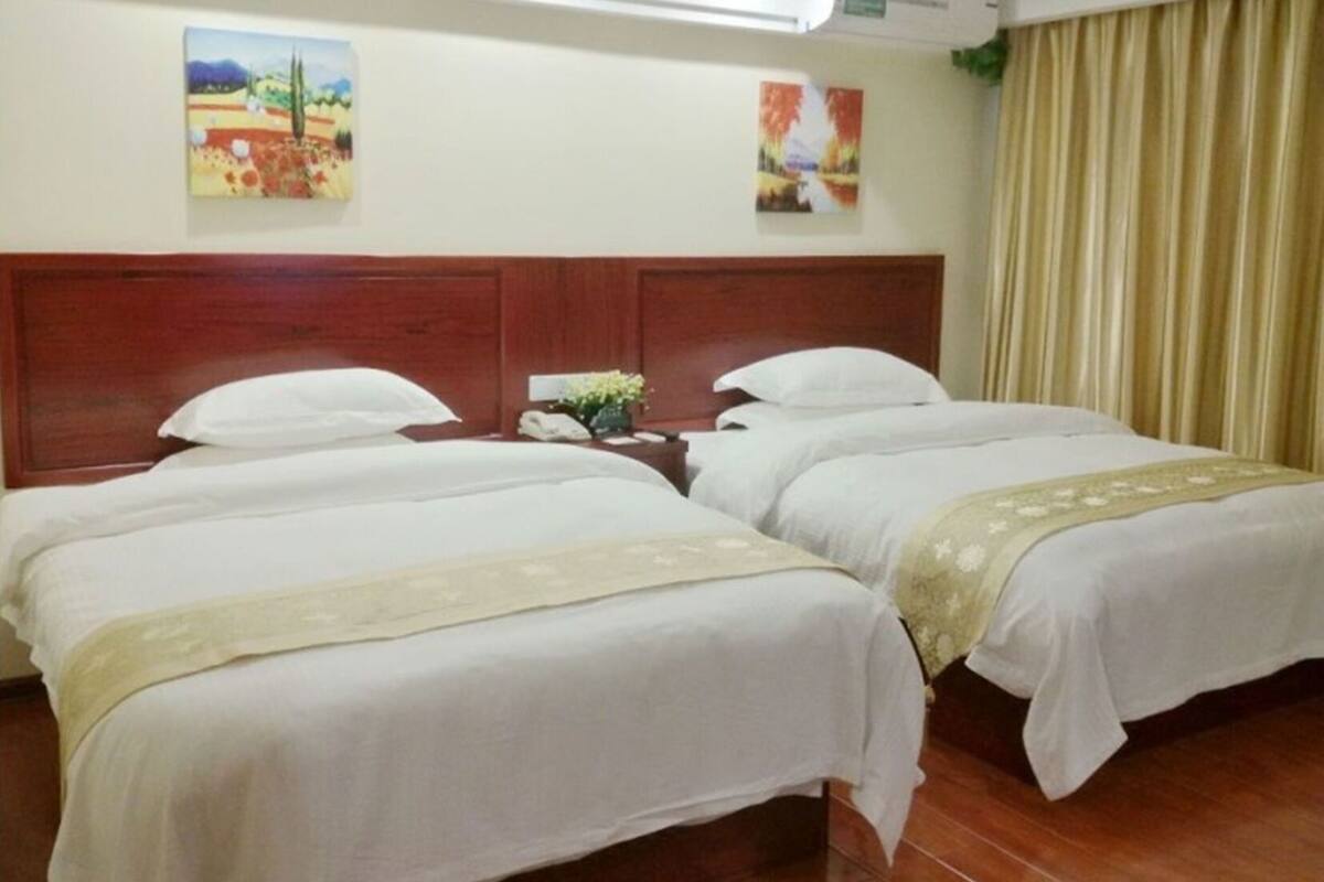 A hotel room with two beds, a wooden headboard, a nightstand with a phone, and two wall art pieces.