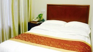A hotel room with a bed, a wooden headboard, a nightstand with a telephone and a plant, and a curtain.