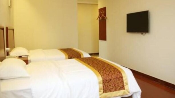 A hotel room with two beds, a television on the wall, and a door leading to another room.