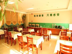Un restaurante con sillas y mesas de madera, una pared verde con caracteres chinos y una zona de bufé con recipientes de comida.