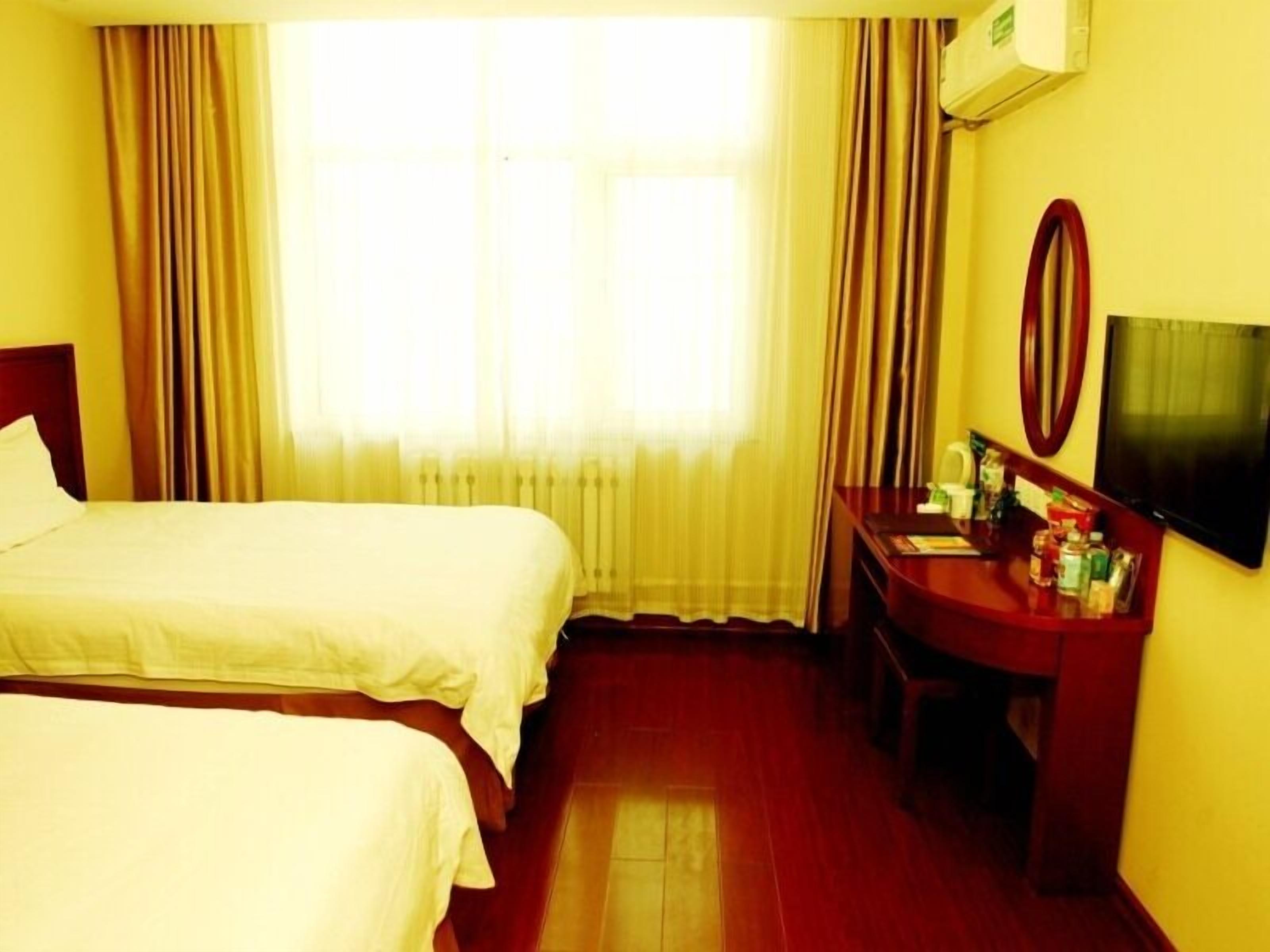 A hotel room with two beds, a desk with a mirror, a television, and a window with curtains.