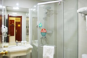 Un baño de hotel con ducha de vidrio, un lavamanos con artículos de aseo y un perchero para toallas.