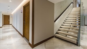 Un couloir d’hôtel moderne avec une porte en bois, un escalier en marbre et une rambarde en verre.