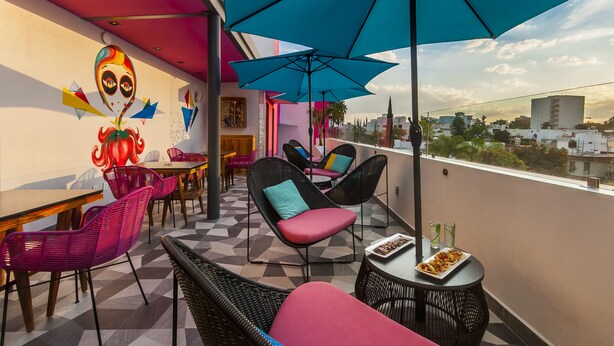 Un balcon avec des chaises colorées, une table sur laquelle se trouve une assiette de nourriture et des parasols bleus.