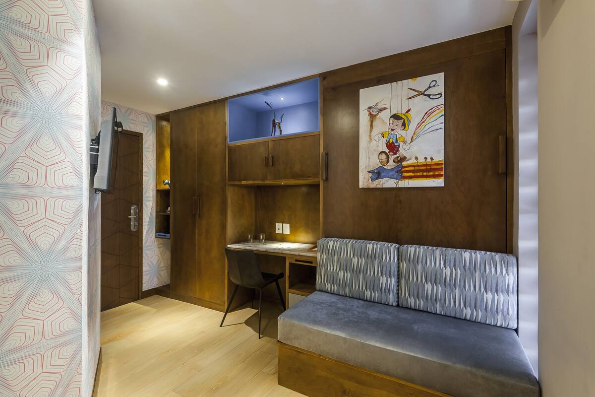 Een compacte kamer met een houten bureau, een gestoffeerde bank en een wandplank.