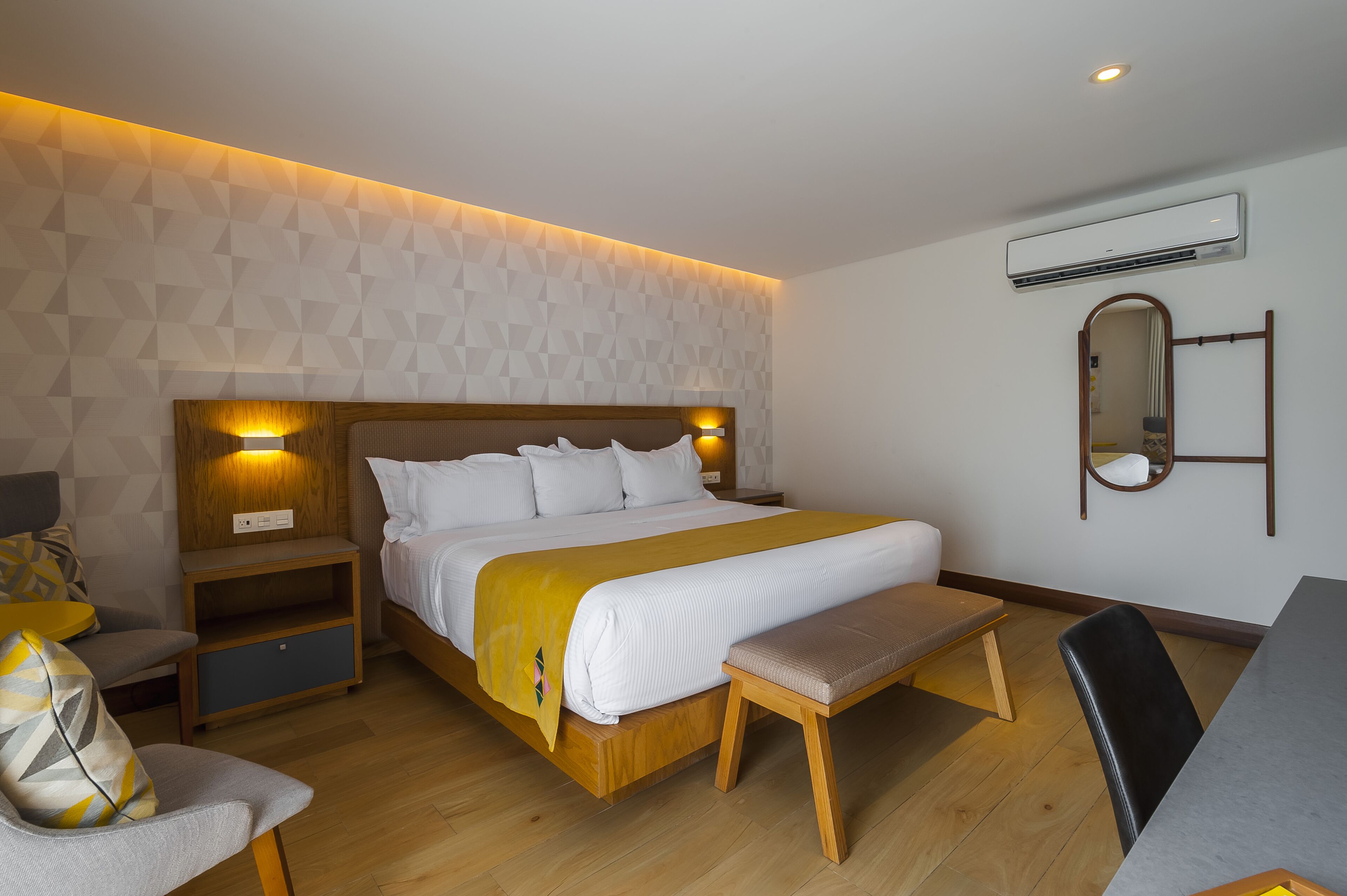 A modern hotel room with a large bed, bedside tables, a bench, and a small seating area.