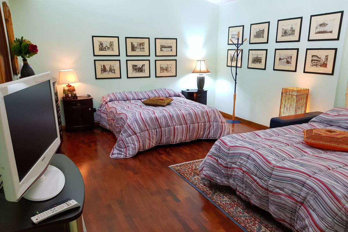A hotel room with two beds, a TV, a lamp, and framed pictures on the wall.
