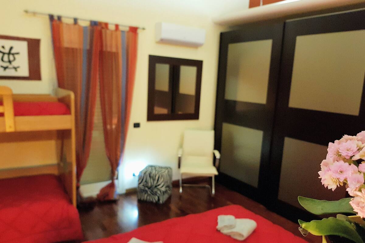 A room with a bunk bed, a chair, a small table, a potted plant, and a sliding door.