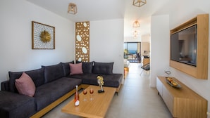 Una sala de estar moderna con un sofá seccional, una mesa de centro de madera con copas de vino, un televisor montado en la pared y un panel decorativo.