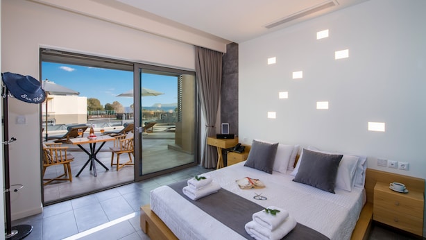 Una habitación de hotel moderna con una cama grande, un balcón con mobiliario exterior y vistas a la ciudad.