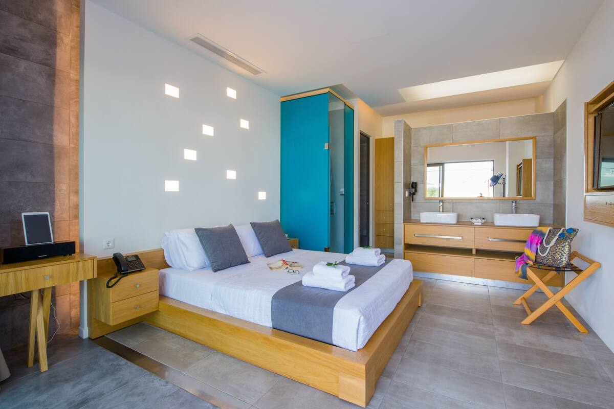 Une chambre moderne comprenant un lit, des tables de chevet, un bureau, une salle de bain avec un miroir et une douche.
