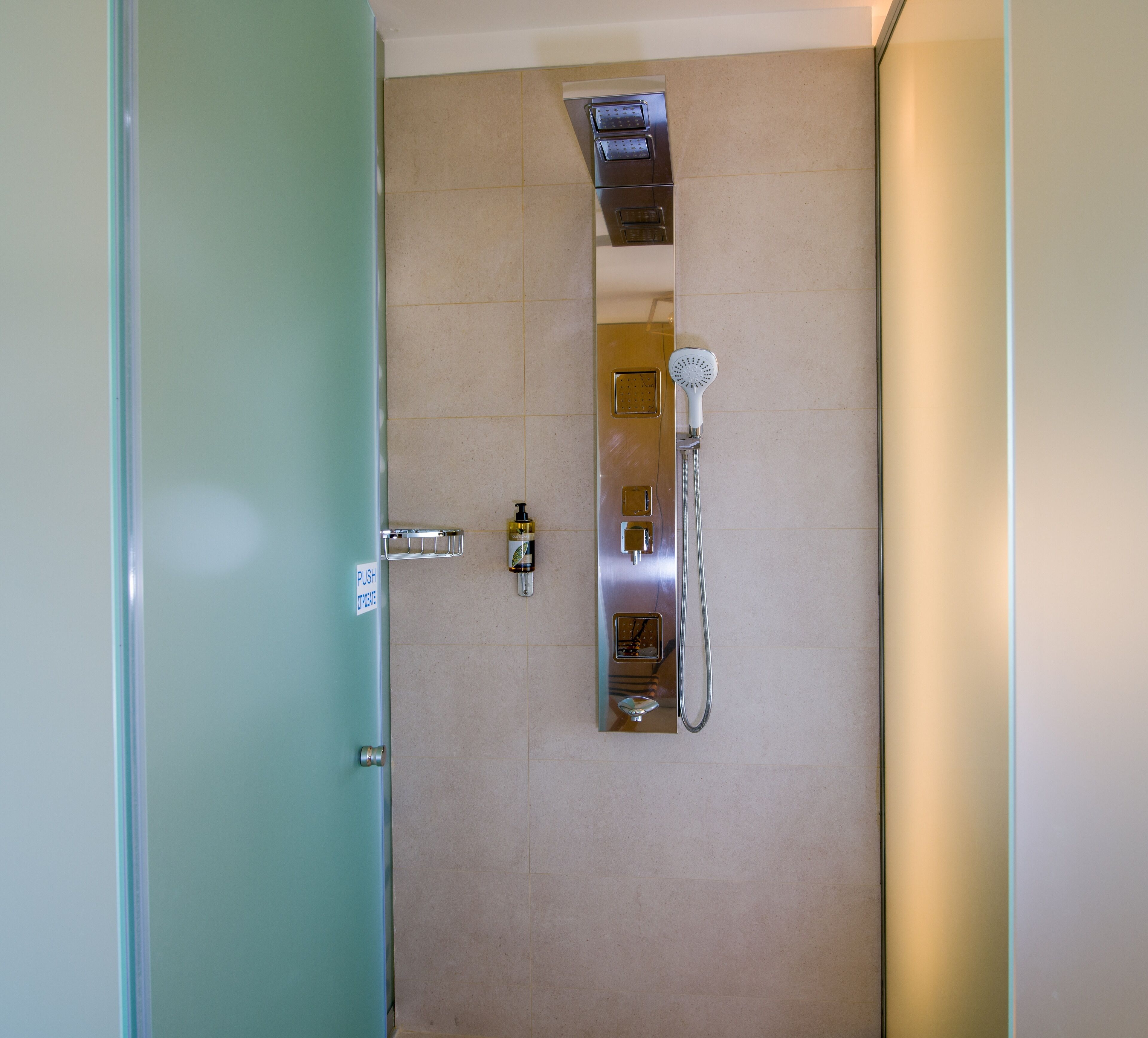 Baño con botón para agua caliente y fría, dispensador de jabón y cabezal de ducha.