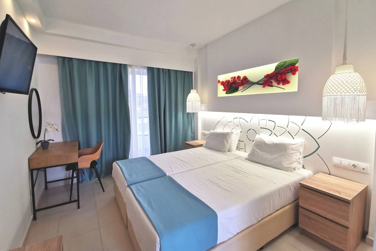 A hotel room with a bed, a desk, a chair, a TV, and a window with curtains.
