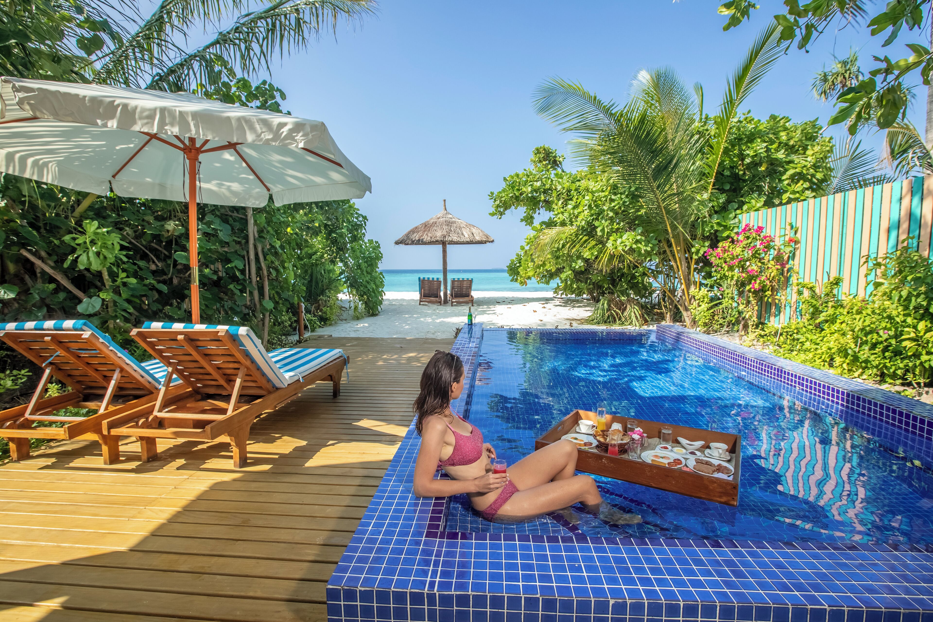 A poolside area with lounge chairs, a table with food and drinks, and a view of the ocean.