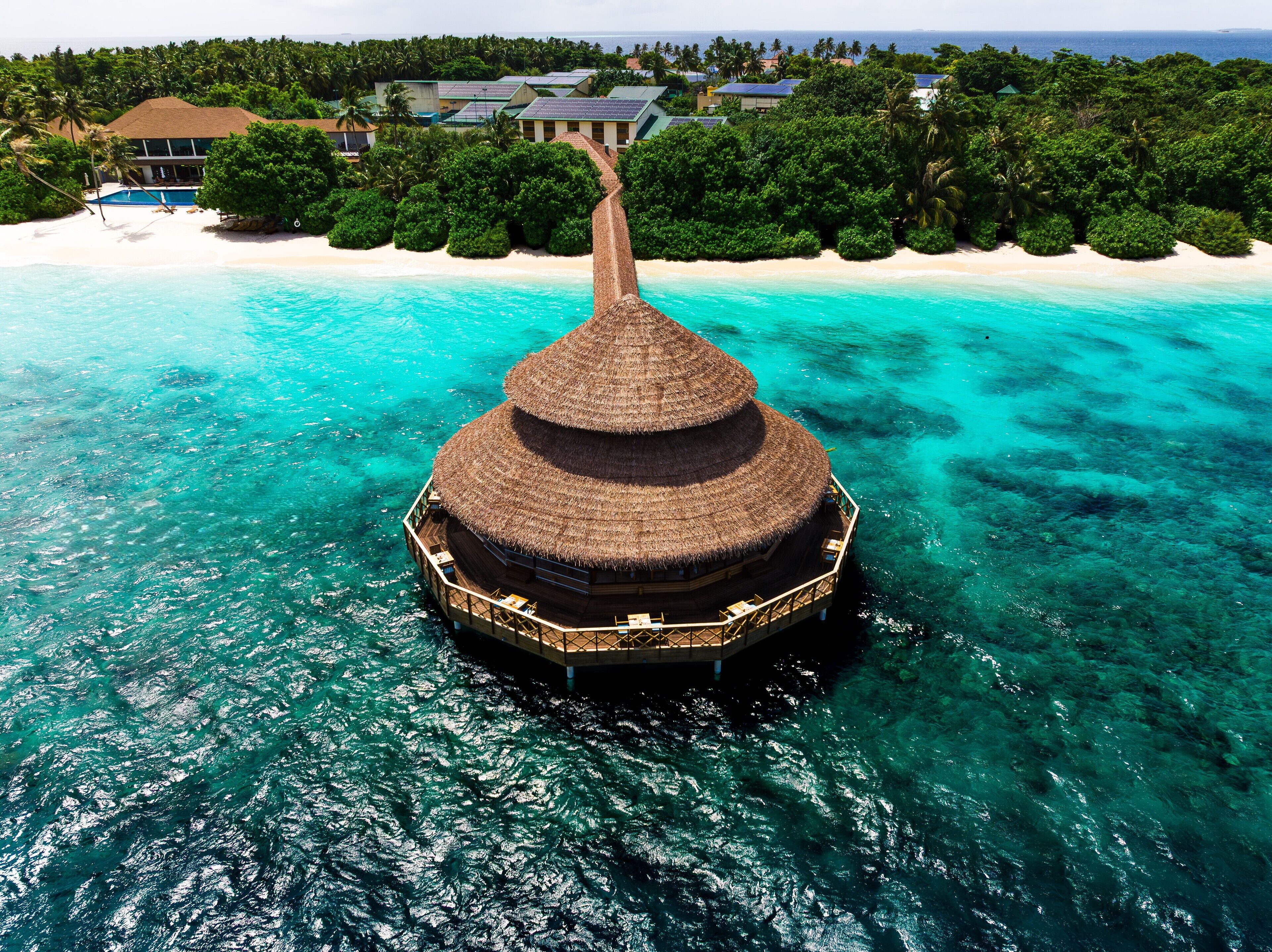 An overwater bungalow with a thatched roof, surrounded by turquoise waters and a sandy beach.