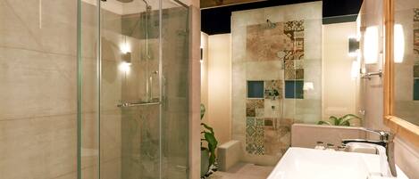 Un baño moderno con ducha de vidrio, un lavamanos grande de color blanco y azulejos decorativos.