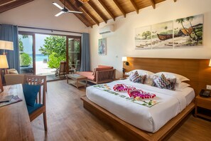 A hotel room with a bed, a desk, a chair, a nightstand, and a view of the beach.
