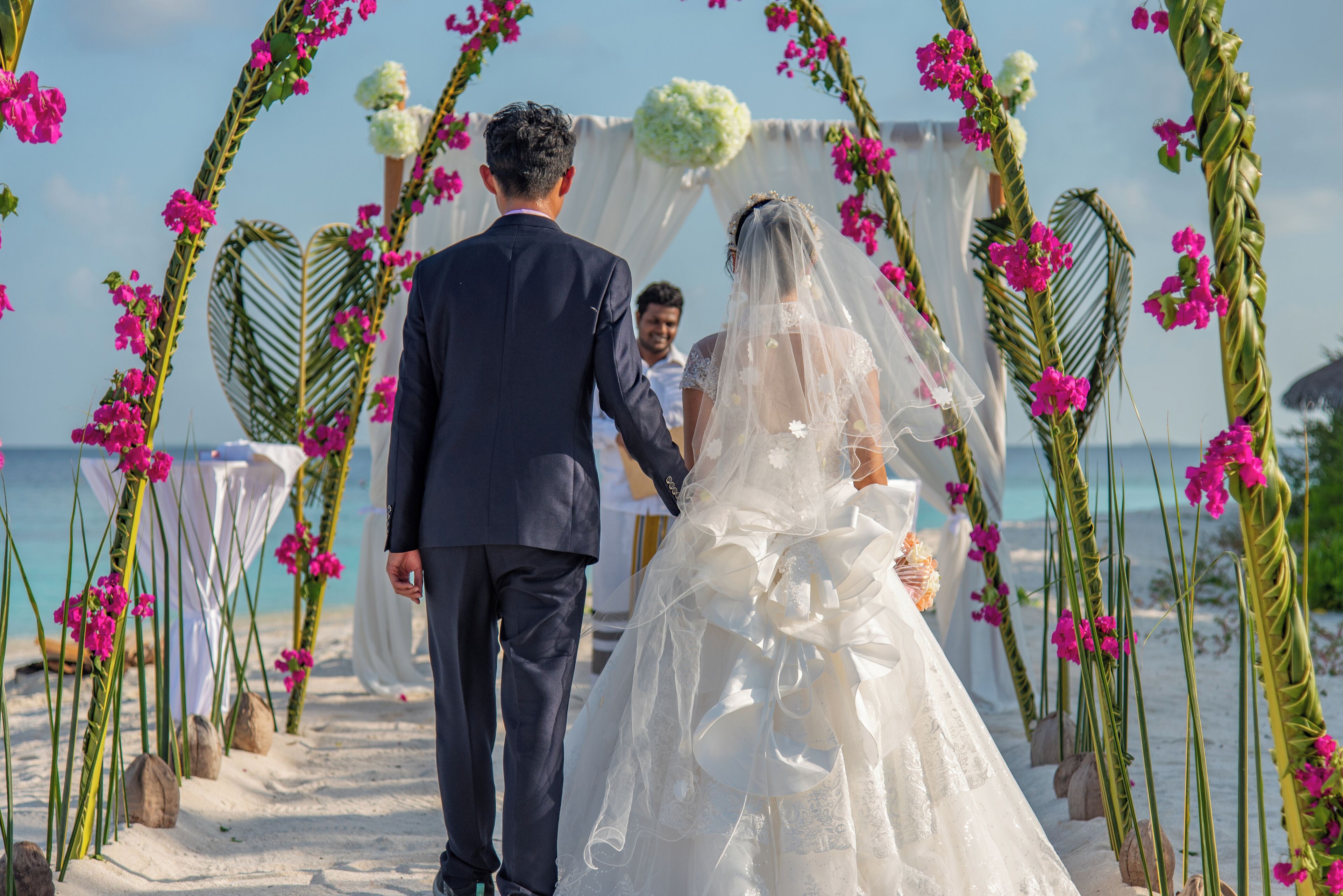 A wedding ceremony on a beach with a white arch and pink flowers.