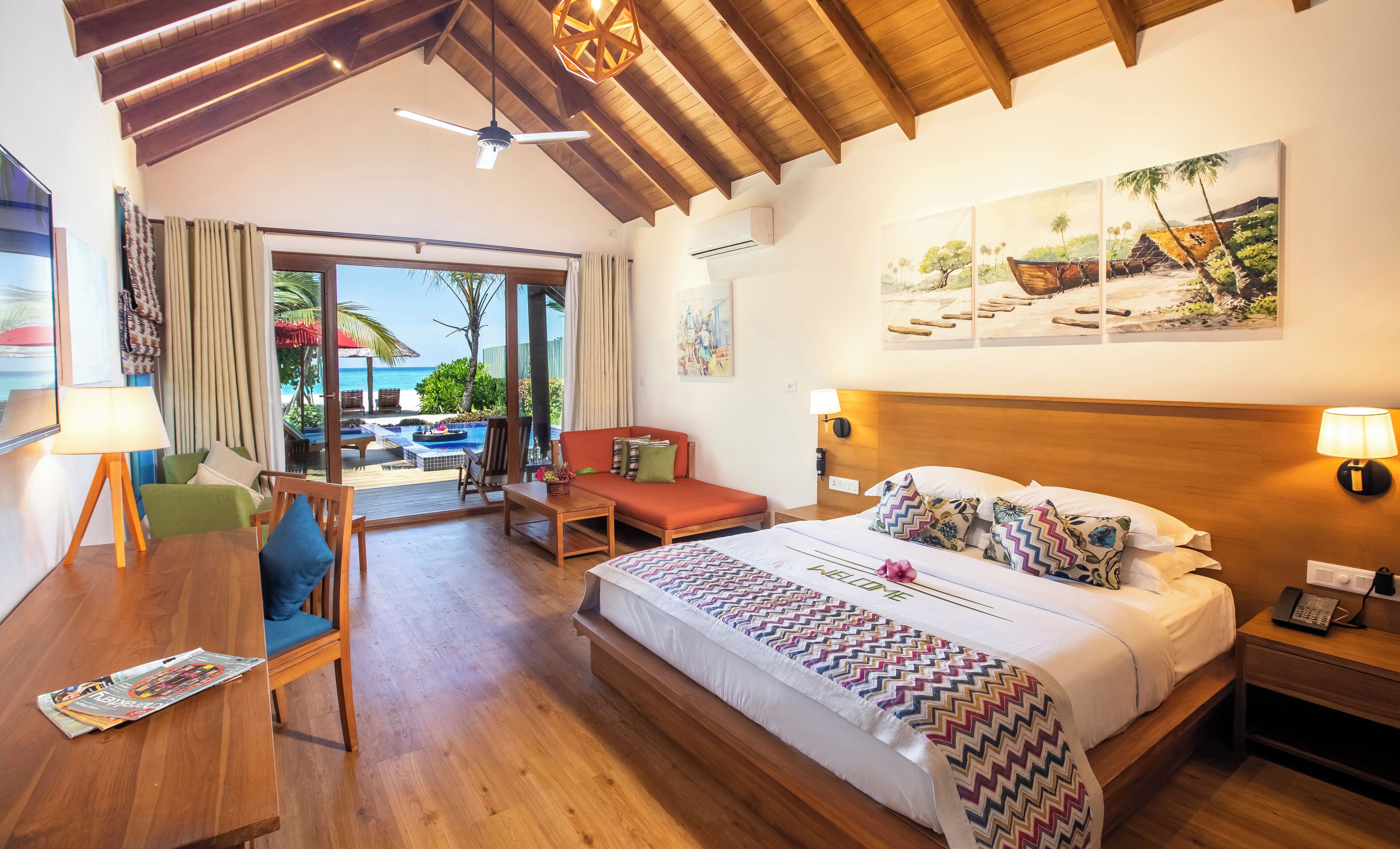Ein Hotelzimmer mit Bett, Schreibtisch, Stuhl, einem kleinen Tisch und Blick auf den Strand.