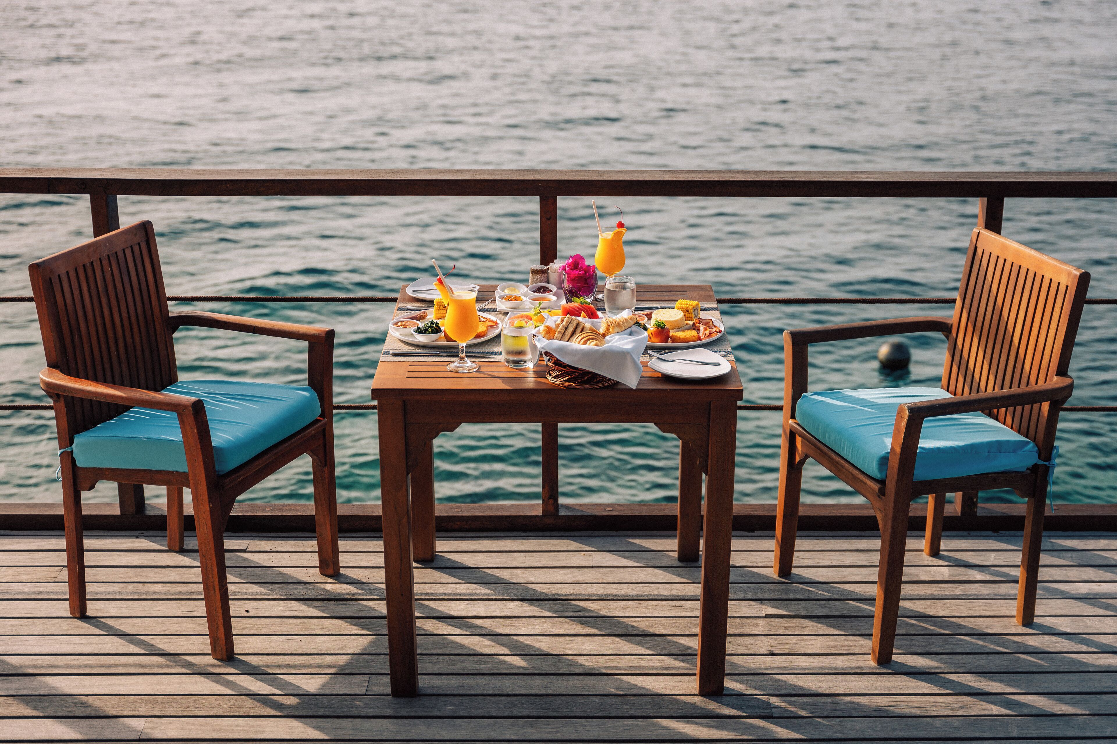 A wooden table with a breakfast spread on a deck overlooking the sea.