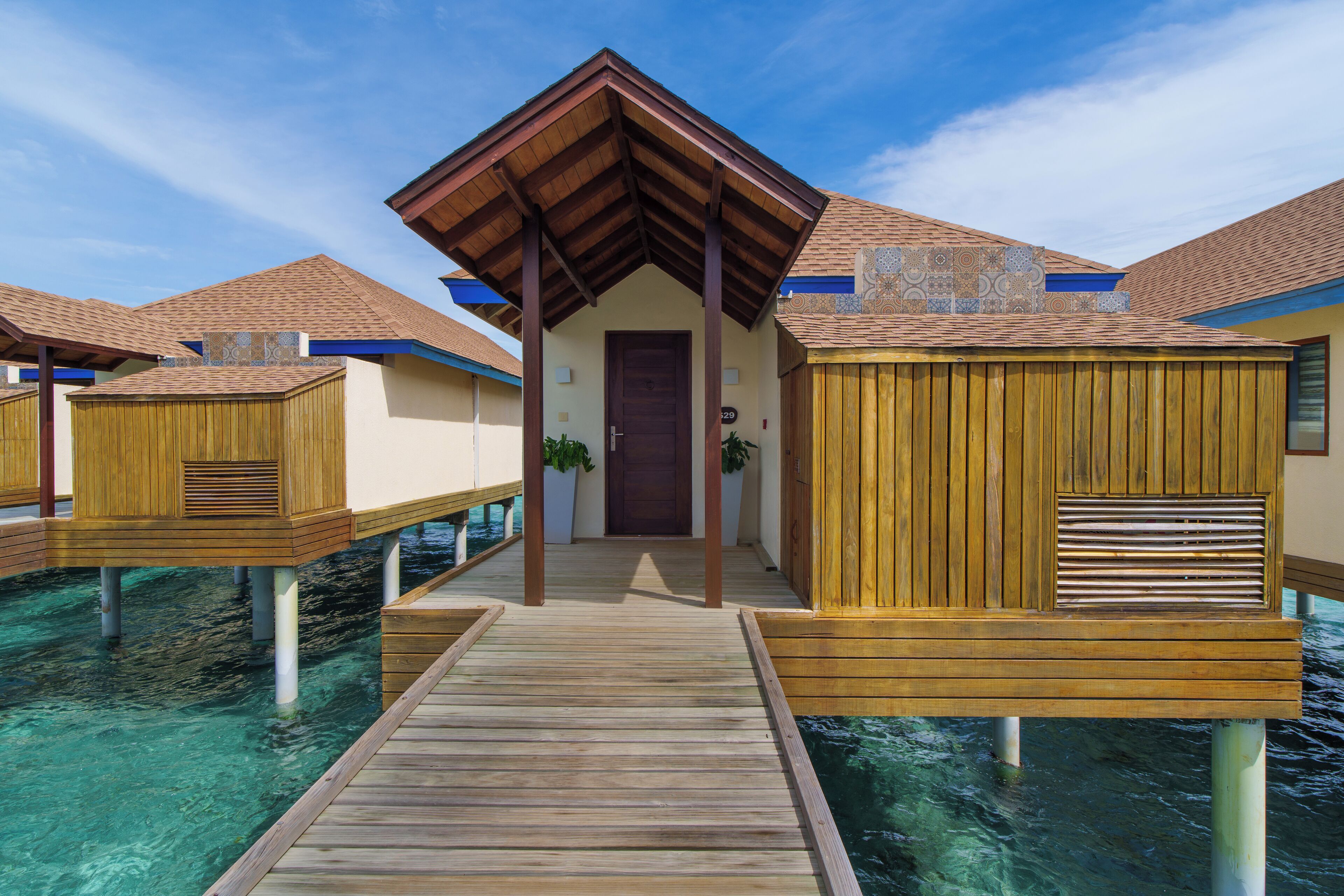 A wooden overwater bungalow with a covered walkway leading to the entrance.