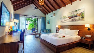A hotel room with a wooden ceiling, a large bed, a desk with a lamp, a chair, a sofa, and a view of greenery outside.
