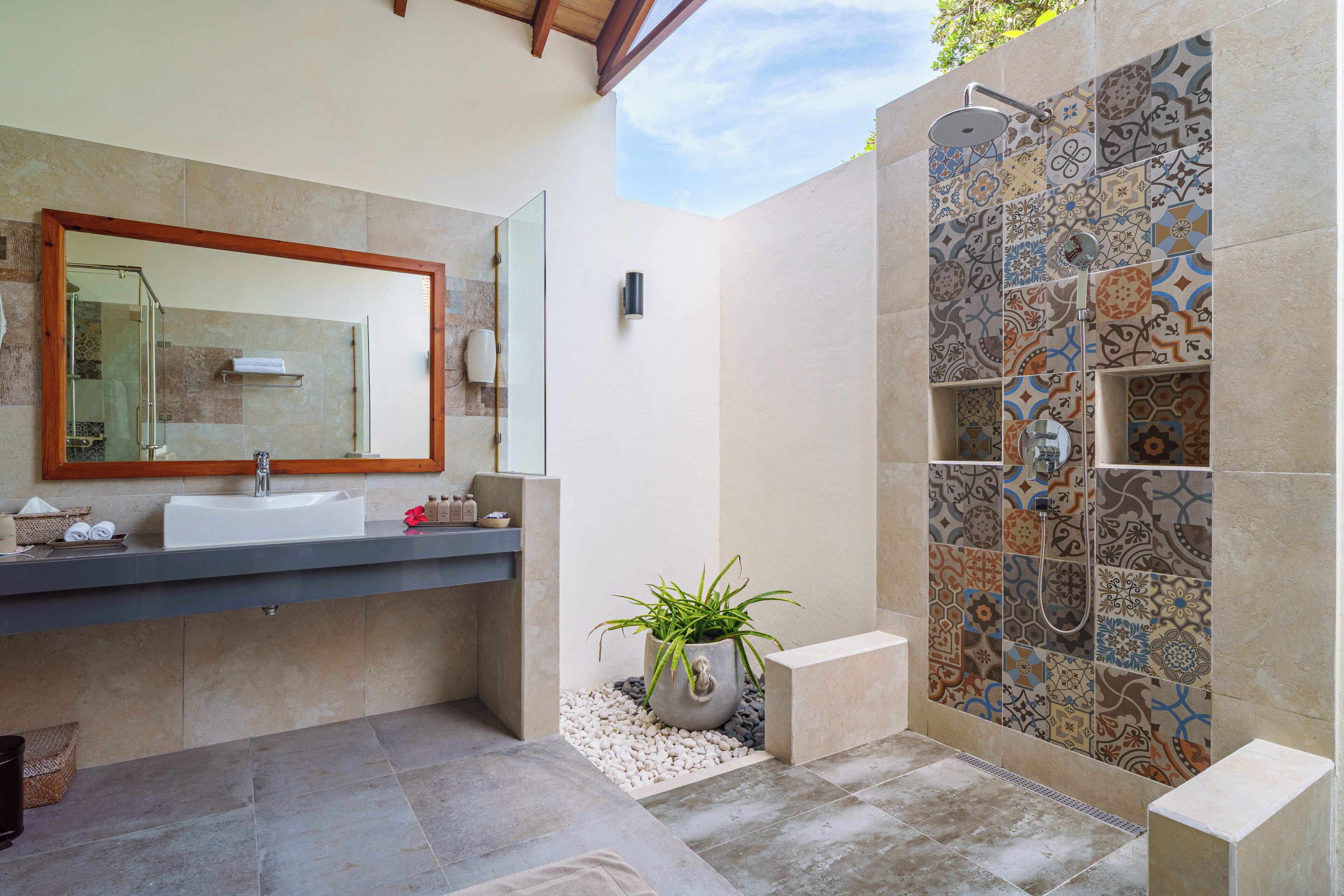 A modern bathroom with a large mirror, a sink, a shower with patterned tiles, and a potted plant.