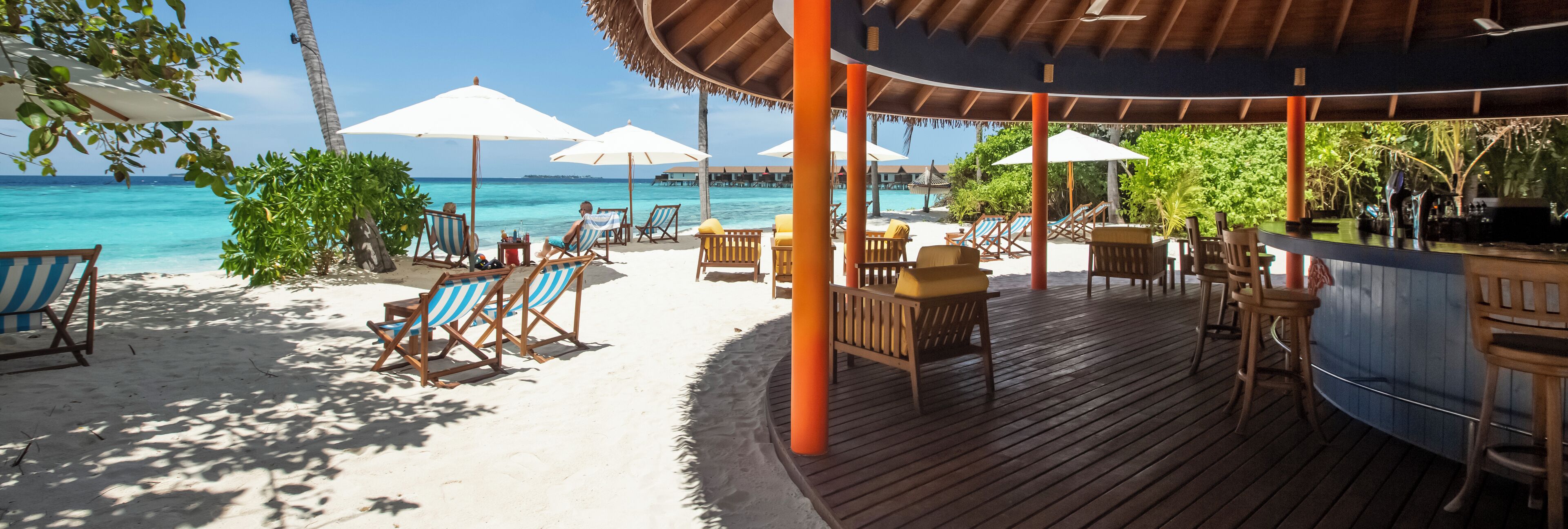 Un espace bar situé au bord de la plage, avec une terrasse en bois, des chaises longues et des parasols.