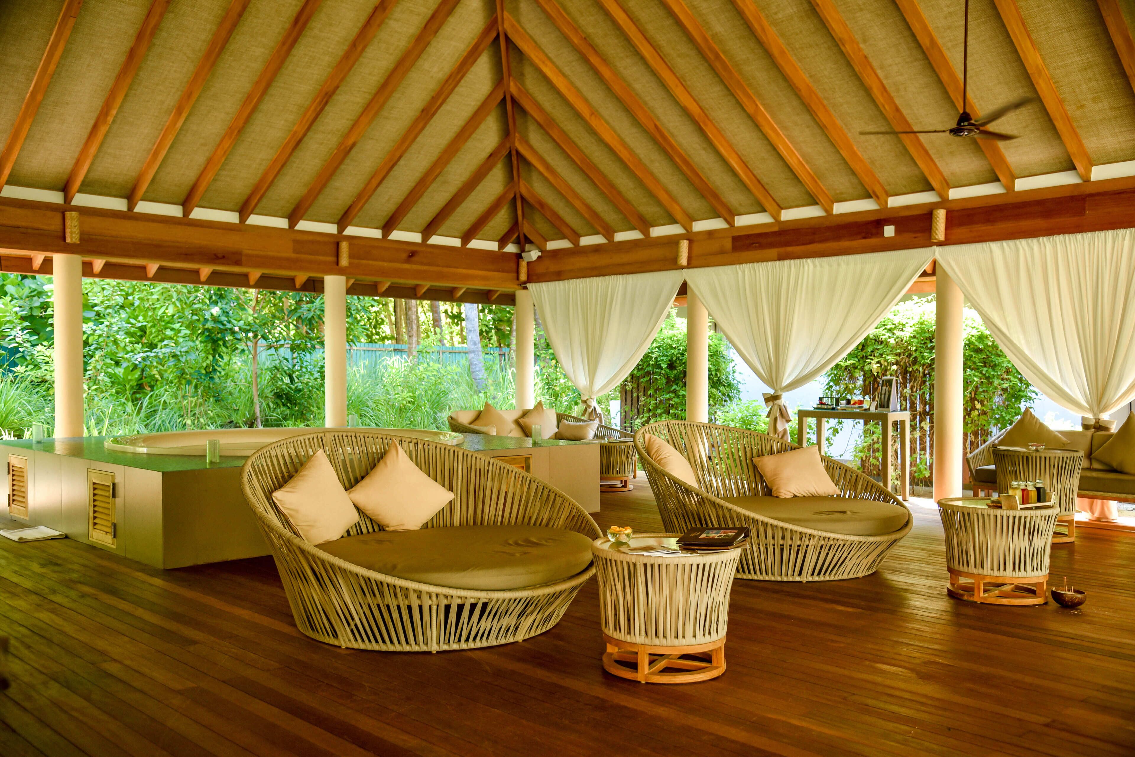 A covered outdoor seating area with wicker furniture and a wooden floor.