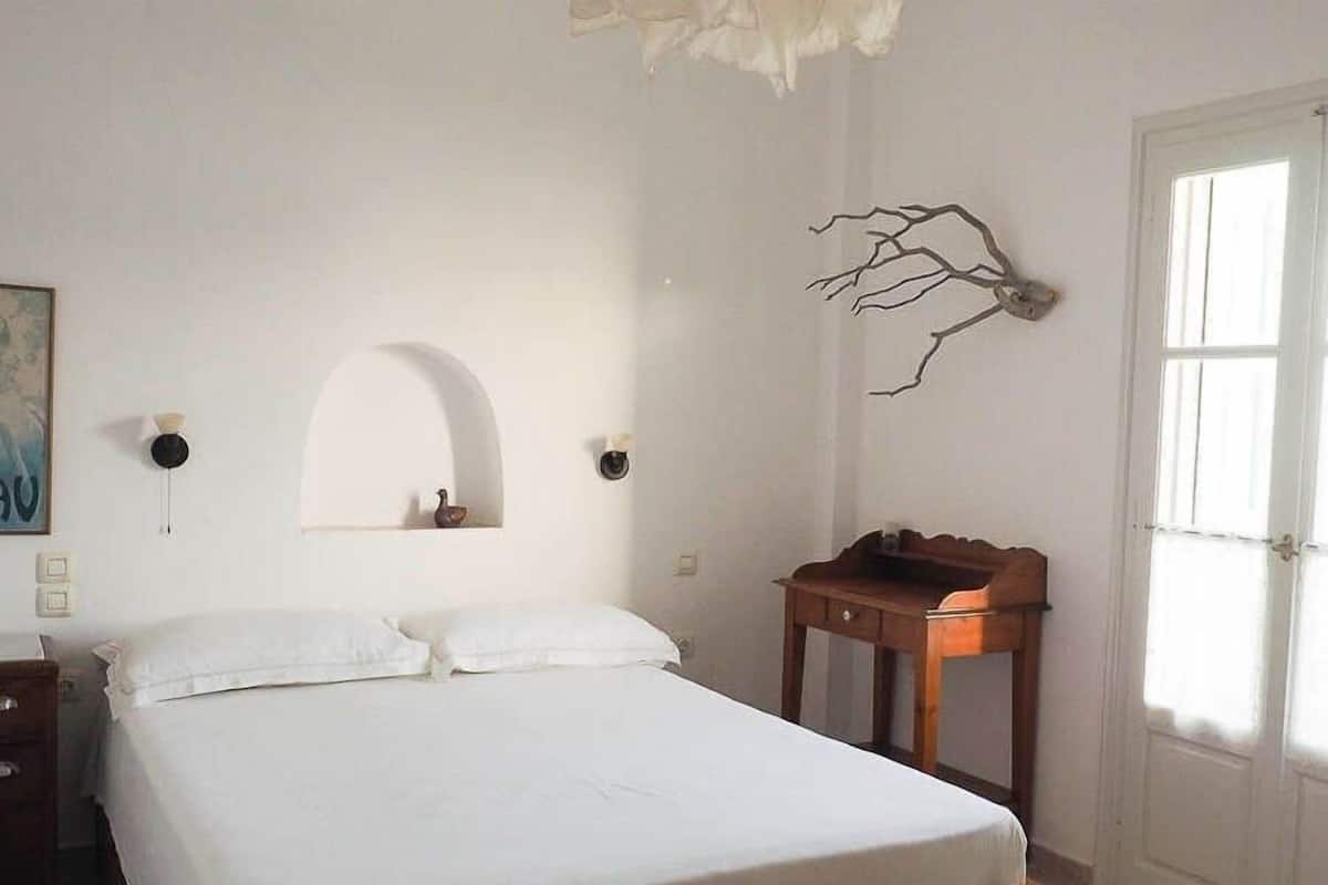 A bedroom with a bed, a wooden nightstand, a wall-mounted shelf, and a door.