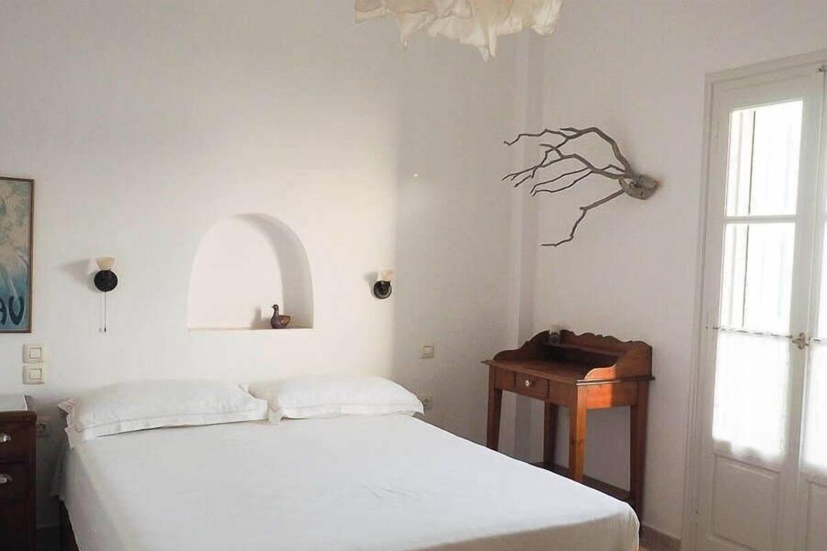 Une chambre à coucher avec un lit, une table de chevet en bois, une étagère fixée au mur et une porte.