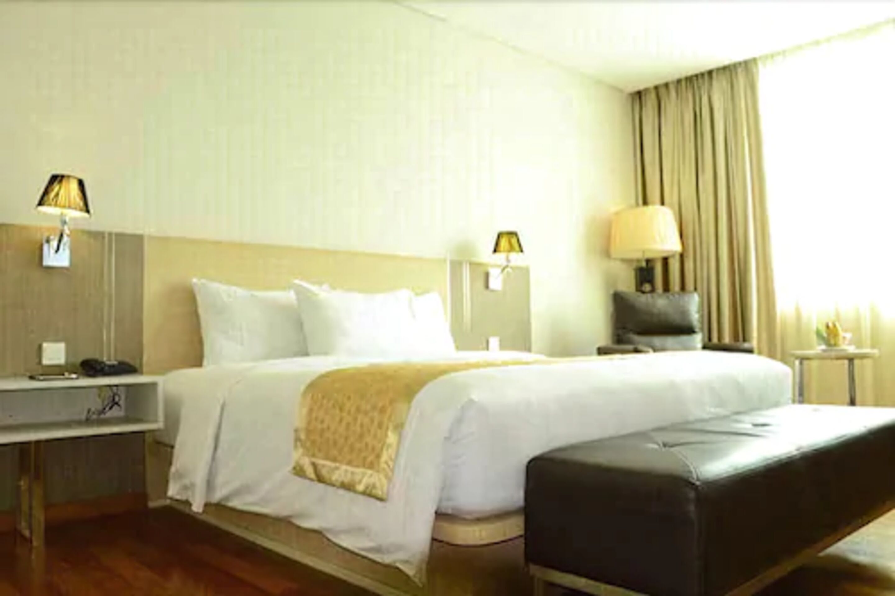 A hotel room with a large bed, two bedside tables with lamps, a desk, and a window with curtains.