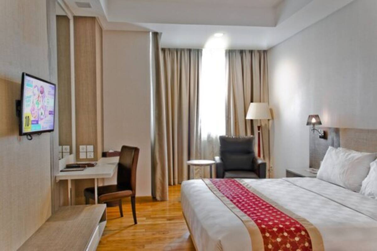 A hotel room with a bed, a desk, a chair, a TV, and a lamp.