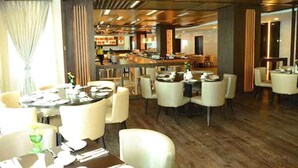 A restaurant with round tables and white chairs, wooden flooring, and a bar area in the background. - Nagoya Hill Hotel Batam (Batam)