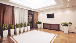 A spacious lobby with a large white carpet, potted plants, a chandelier, and a flat-screen TV on the wall. - Familion Aparthotel (Chisinau)