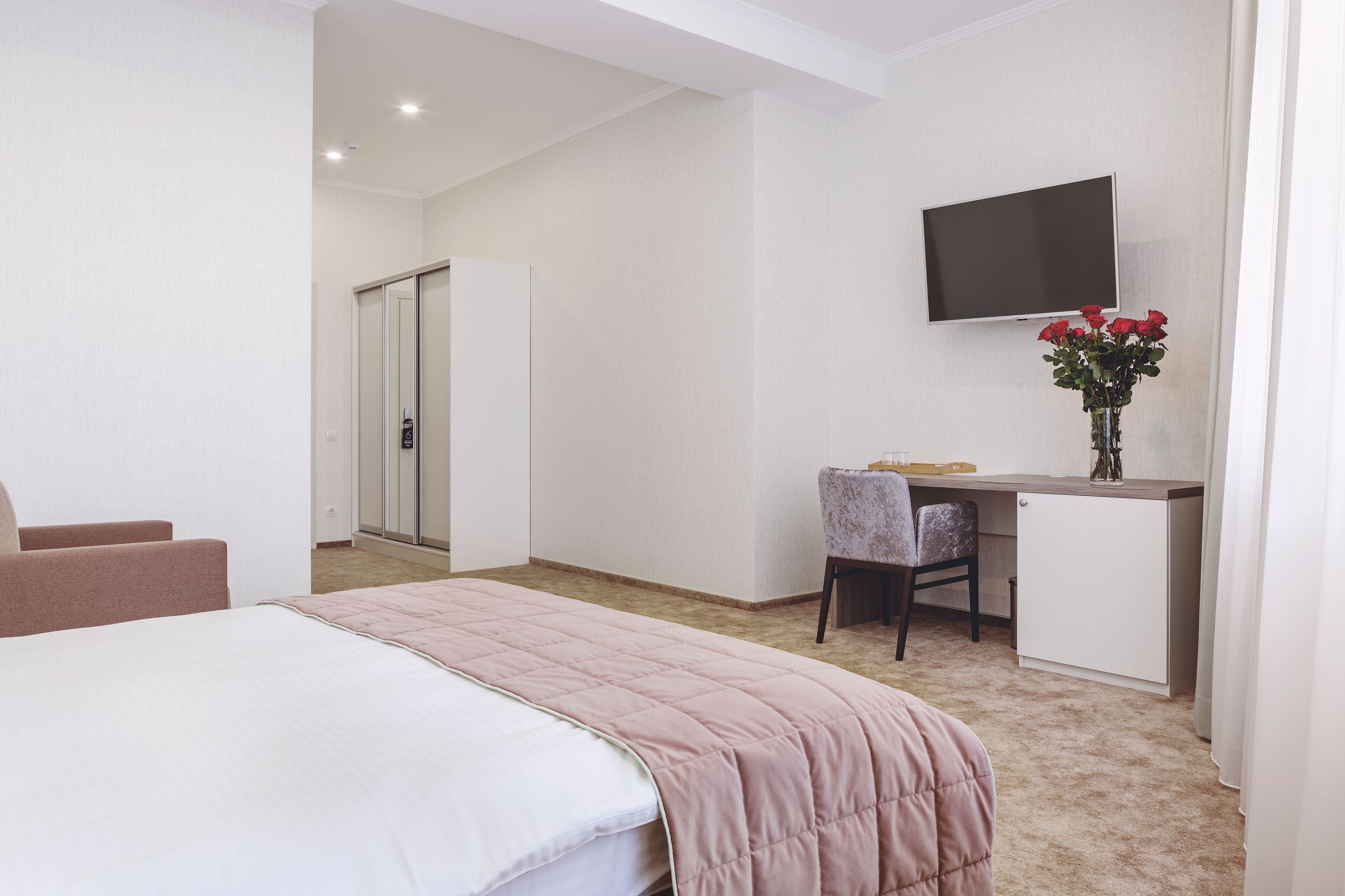 Habitación de hotel con cama, escritorio, silla, televisión y un florero con flores.