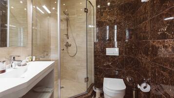 Un baño moderno con cabina de ducha de vidrio, un lavamanos blanco con espejo y pared revestida de mármol.