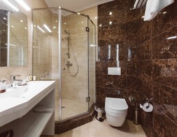 Un baño moderno con cabina de ducha de vidrio, un lavamanos blanco con espejo y pared revestida de mármol.