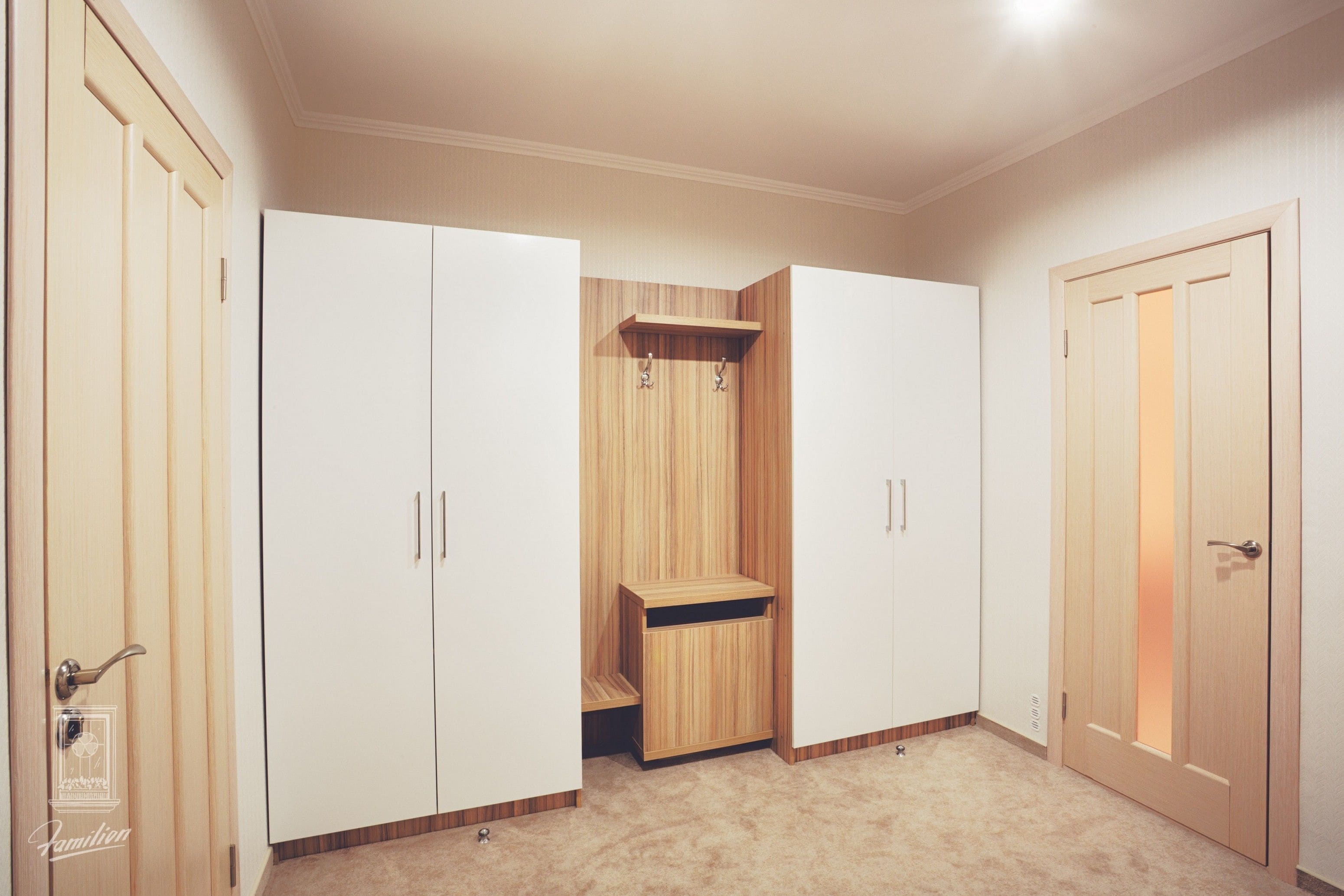 Una habitación con armarios blancos, un aparador de madera y una puerta con panel iluminado.