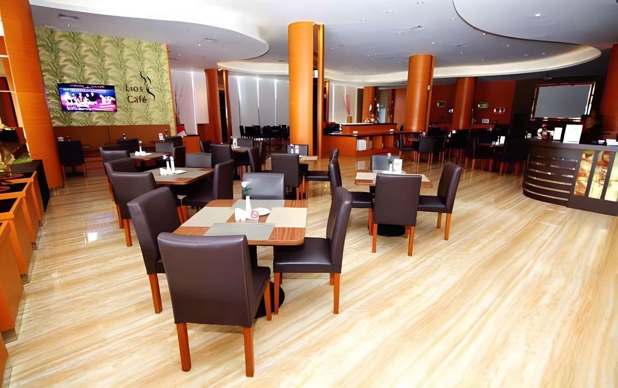A modern restaurant with multiple dining tables and chairs, a bar area, and a television screen displaying a program.