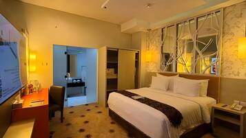 A hotel room with a bed, bedside table, TV, desk, chair, and a wardrobe.