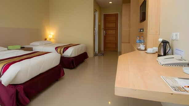A hotel room with two beds, a wooden desk with a coffee maker, and a door leading to another room. - Bangka City Hotel (Pangkalpinang)