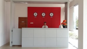 En receptionsdisk med en röd panel och tre klockor, en trädörr och en vas med blommor.
