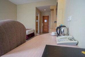 Une chambre d’hôtel comprenant un lit, un bureau avec un téléphone et une bouilloire, ainsi qu’une porte donnant sur une autre pièce.