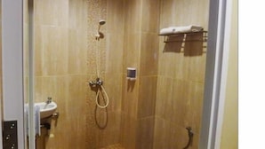 A shower area with a handheld showerhead, a towel rack with towels, and a small shelf with toiletries. - Bangka City Hotel (Pangkalpinang)