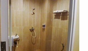 A shower area with a handheld showerhead, a towel rack with towels, and a small shelf with toiletries. - Bangka City Hotel (Pangkalpinang)
